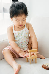 Toddler sitting and playing in Avauma apricot daisy tank top and pink shorts